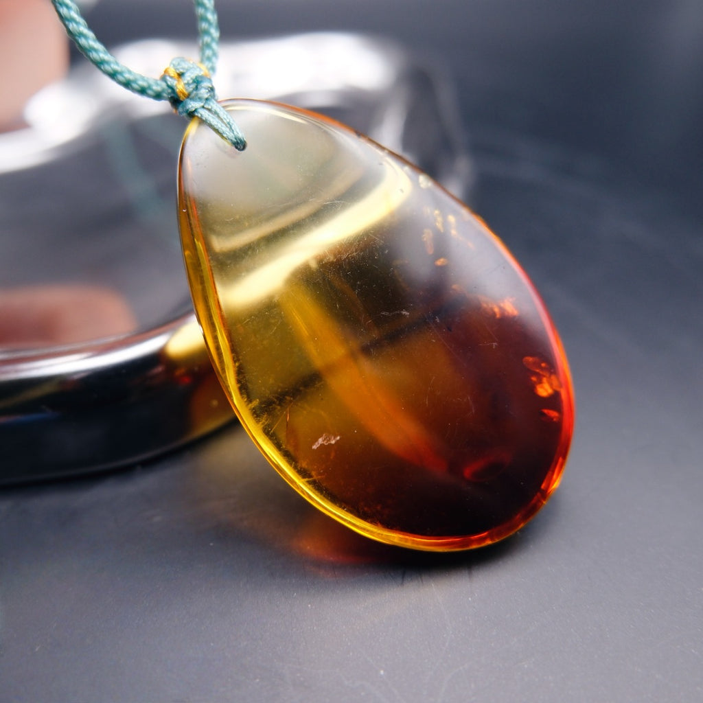 Pendant: transparent Baltic amber teardrop, yellow shading to dark red, golden flakes, teal cord, side view