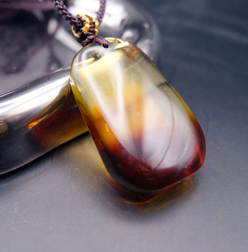 Pendant: transparent Baltic amber, yellow top shading to a dark red base, rounded rectangle, dark cord, leaning on a tray