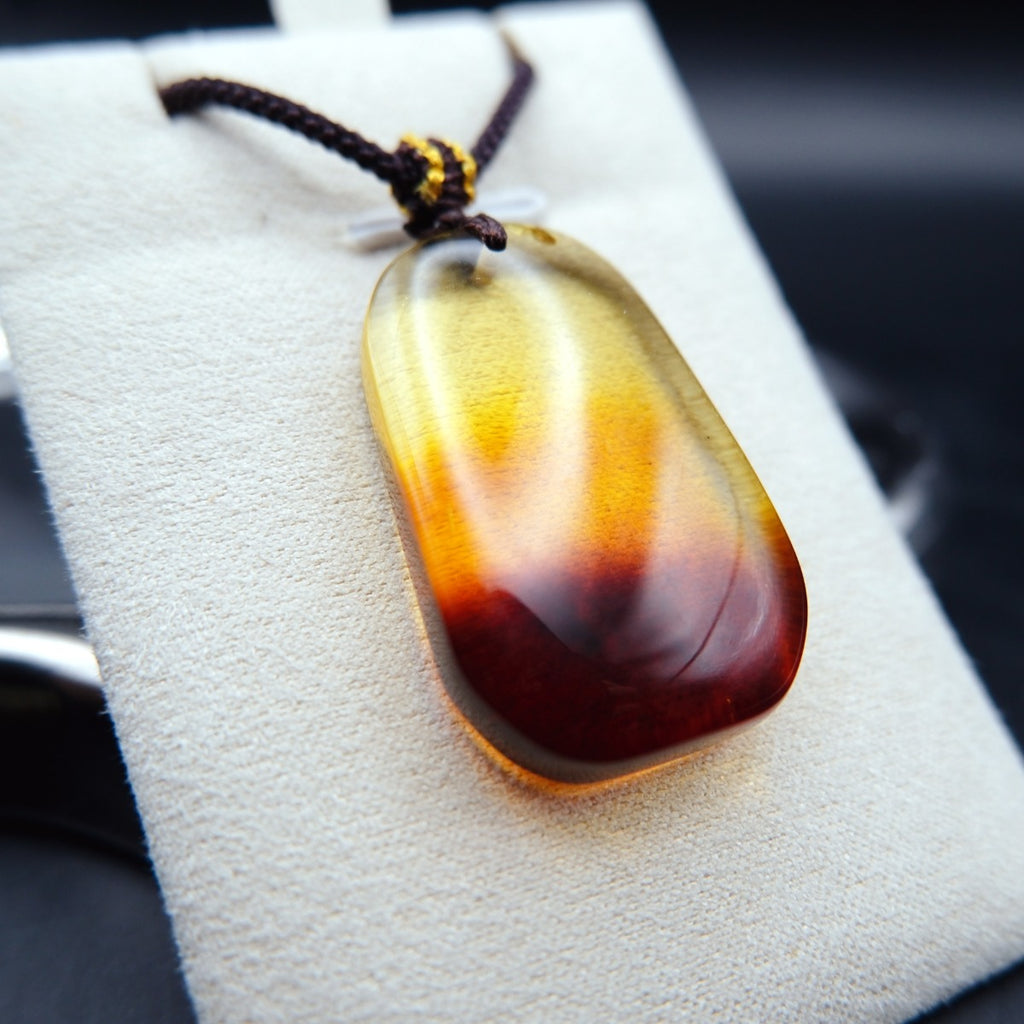 Pendant: transparent Baltic amber, yellow top shading to a dark red base, rounded rectangle, dark cord, on a grey stand