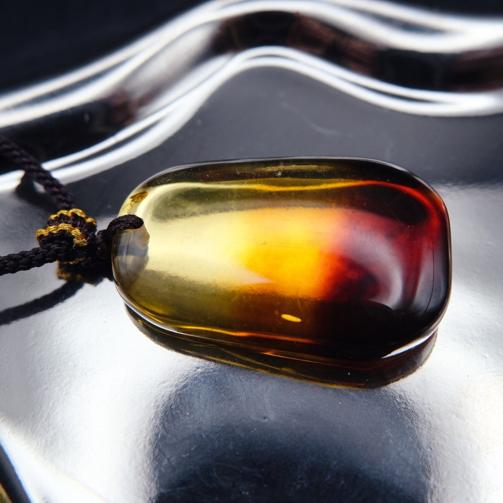 Pendant: transparent Baltic amber, yellow top shading to a dark red base, rounded rectangle, dark cord, lying flat