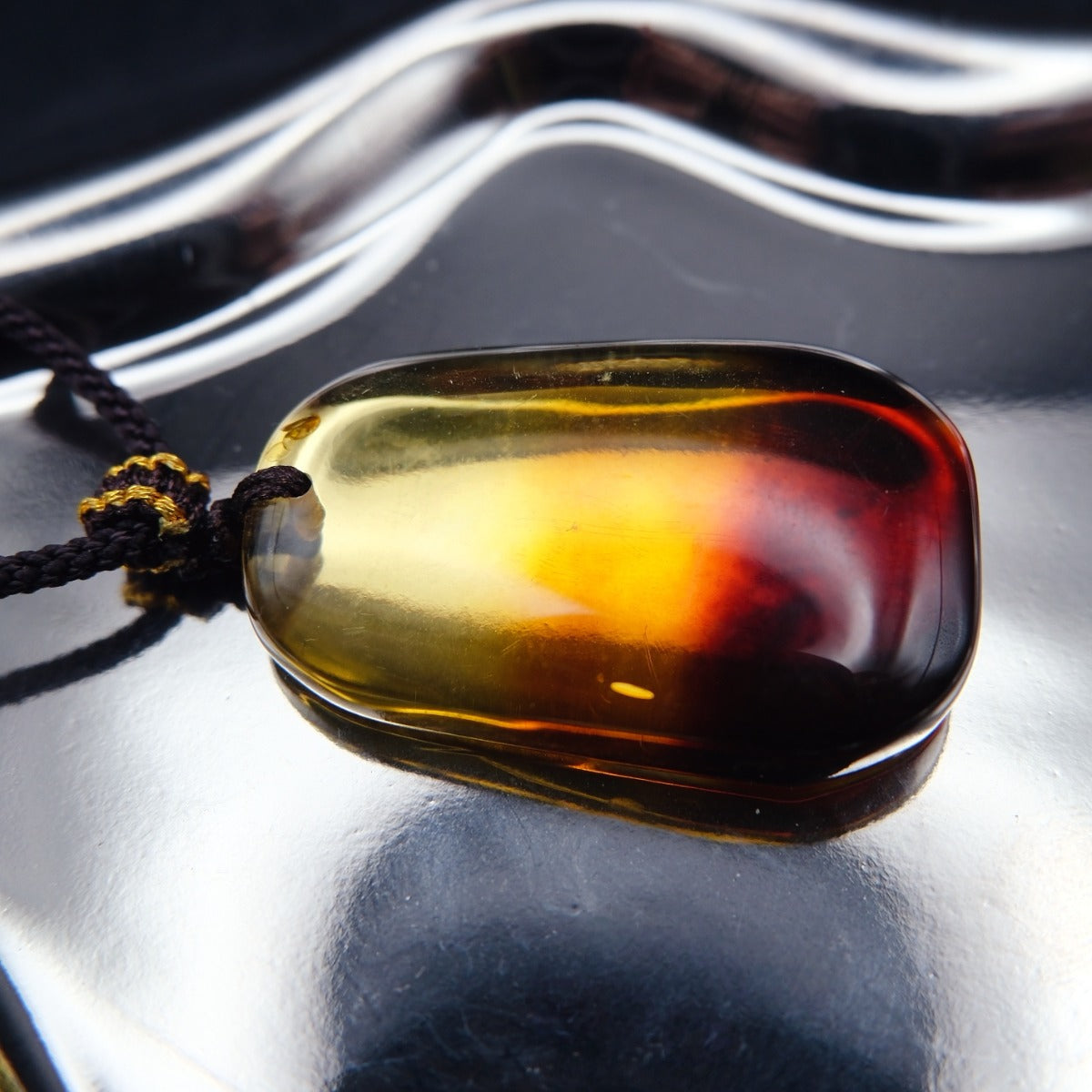 Pendant: transparent Baltic amber, yellow top shading to a dark red base, rounded rectangle, dark cord, lying flat