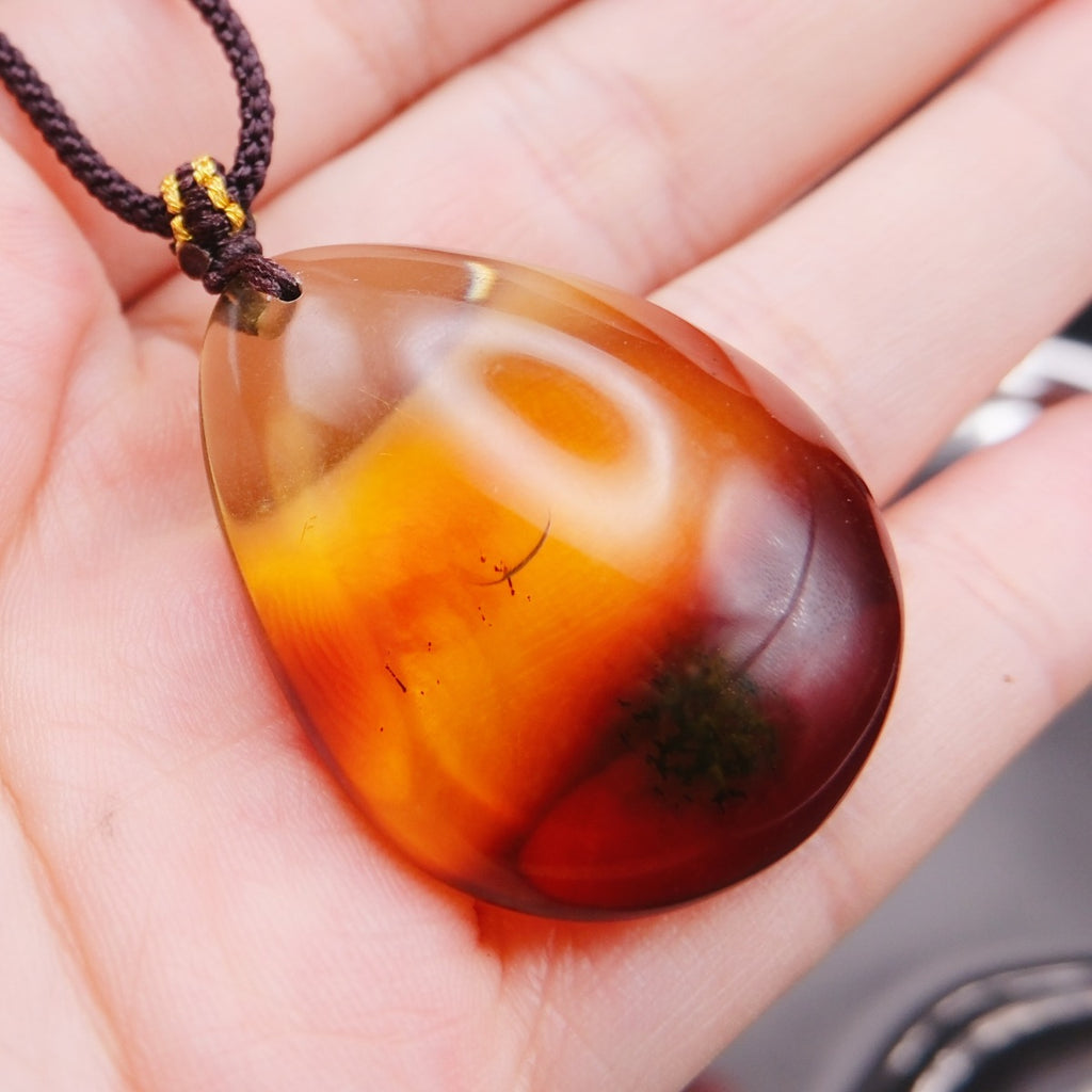 Pendant: transparent Baltic amber teardrop, orange-yellow shading to dark red, dark cord, on an open palm