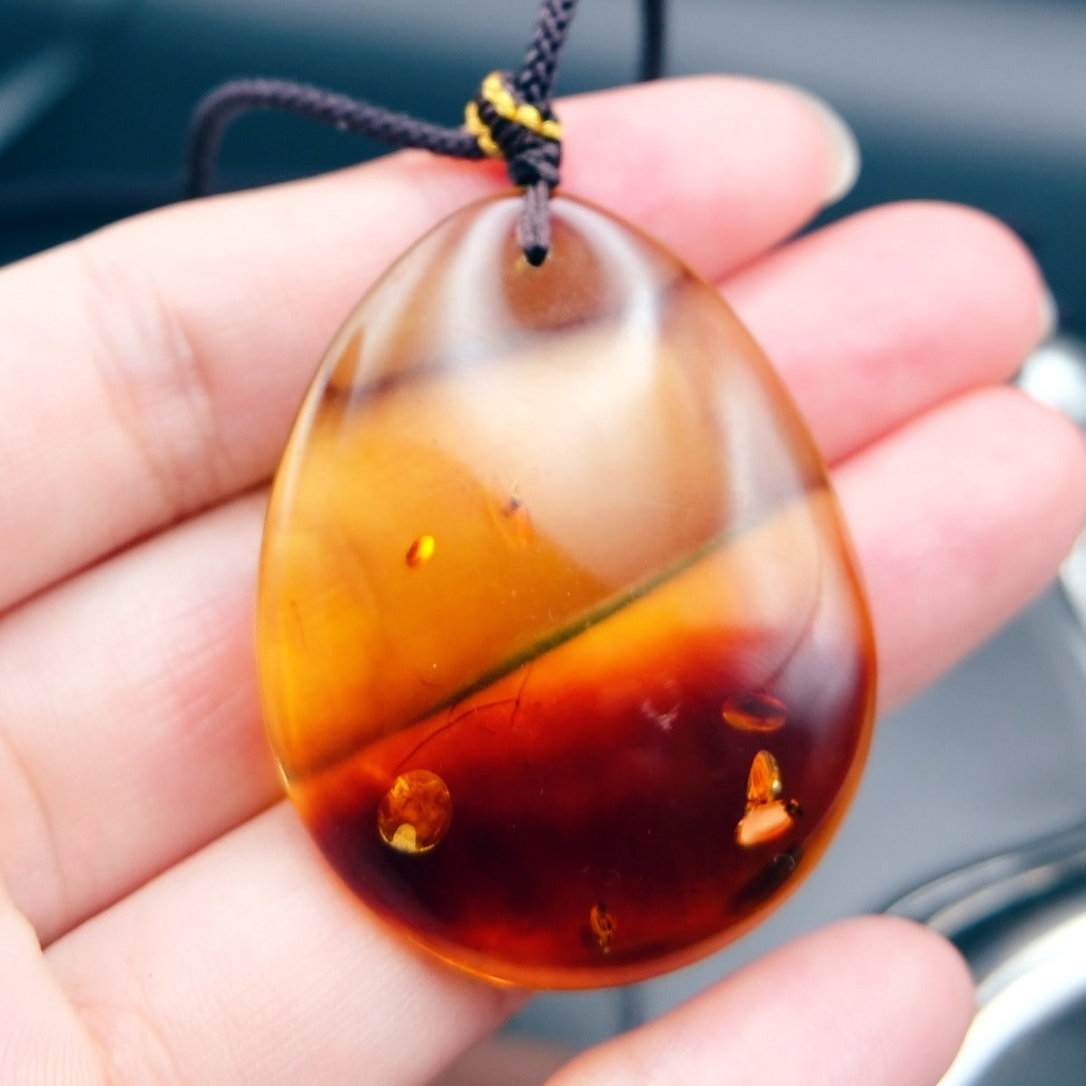 Pendant: transparent Baltic amber teardrop, yellow top and dark red lower half, dark cord, on an open palm