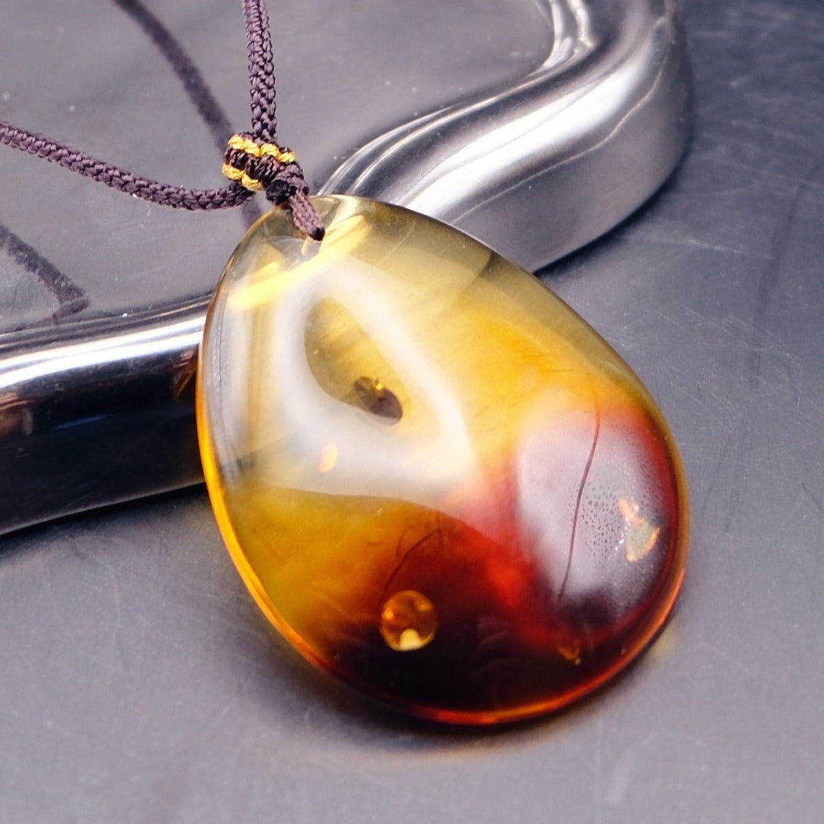 Pendant: transparent Baltic amber teardrop, yellow top and dark red lower half, dark cord, second angle
