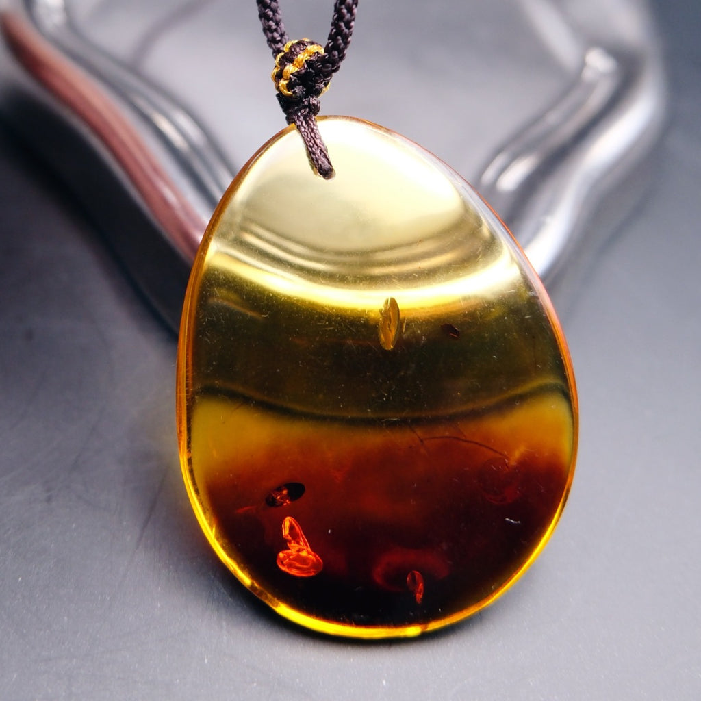 Pendant: transparent Baltic amber teardrop, yellow top and dark red lower half, dark cord, standing, front view