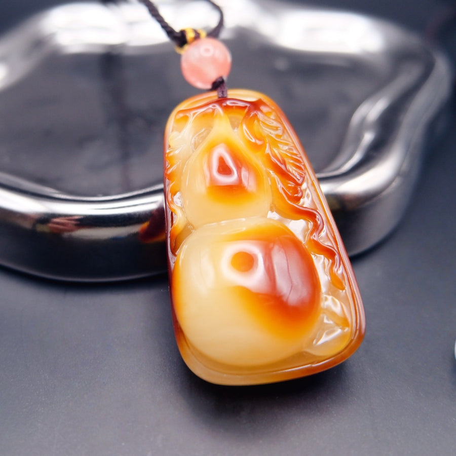 Pendant: Baltic amber carved as a gourd, cream to orange-brown, with a pink bead on a dark cord